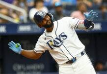 Rays Star Makes MLB History After Latest Home Run Baseball player in a white uniform with blue accents and blue gloves reaches forward during a play, wearing a dark helmet.