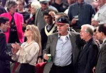 Media Billionaire And Former Braves Owner Dies at 87 Crowd at a public event; a man in a baseball cap holds a green cup and chats with others nearby.