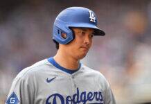 Shohei Ohtani Exits Dodgers Game With Scary Injury Baseball player wearing a blue Dodgers helmet and gray uniform, looking to the right with a blurred stadium background.