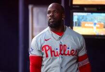 Phillies Outfield Left With Huge Void After Latest Injury Portrait of a Black man wearing a Philadelphia Phillies baseball jersey with a silver chain, indoors.