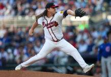 Forgotten Braves Pitcher Could Rejoin The Team Soon Baseball pitcher in a Braves uniform mid-pitch on the mound with a blurred crowd in the stands behind him.